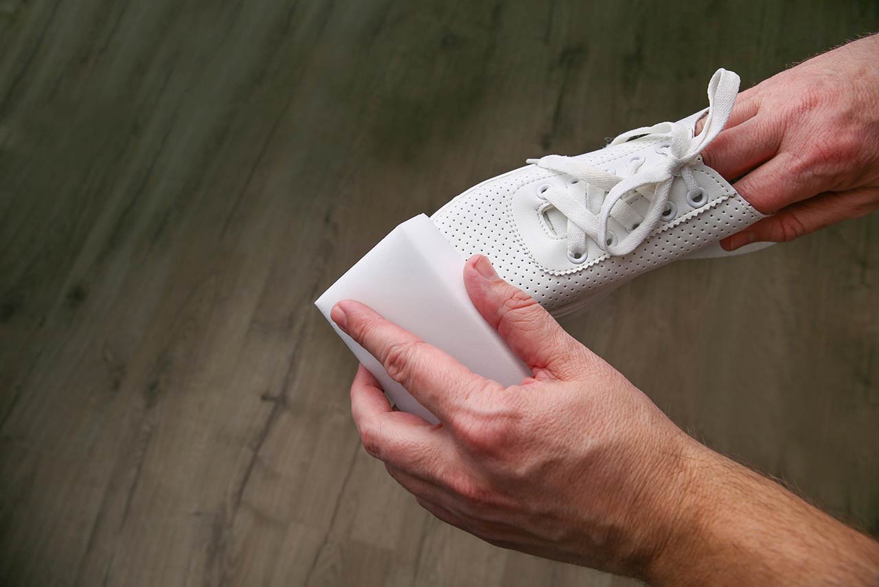 Photo of a man cleaning white sneakers with melamine sponge