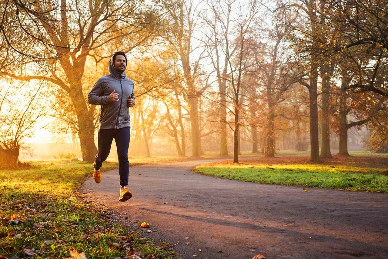 Photo of an adult male runner in park at autumn sunrise