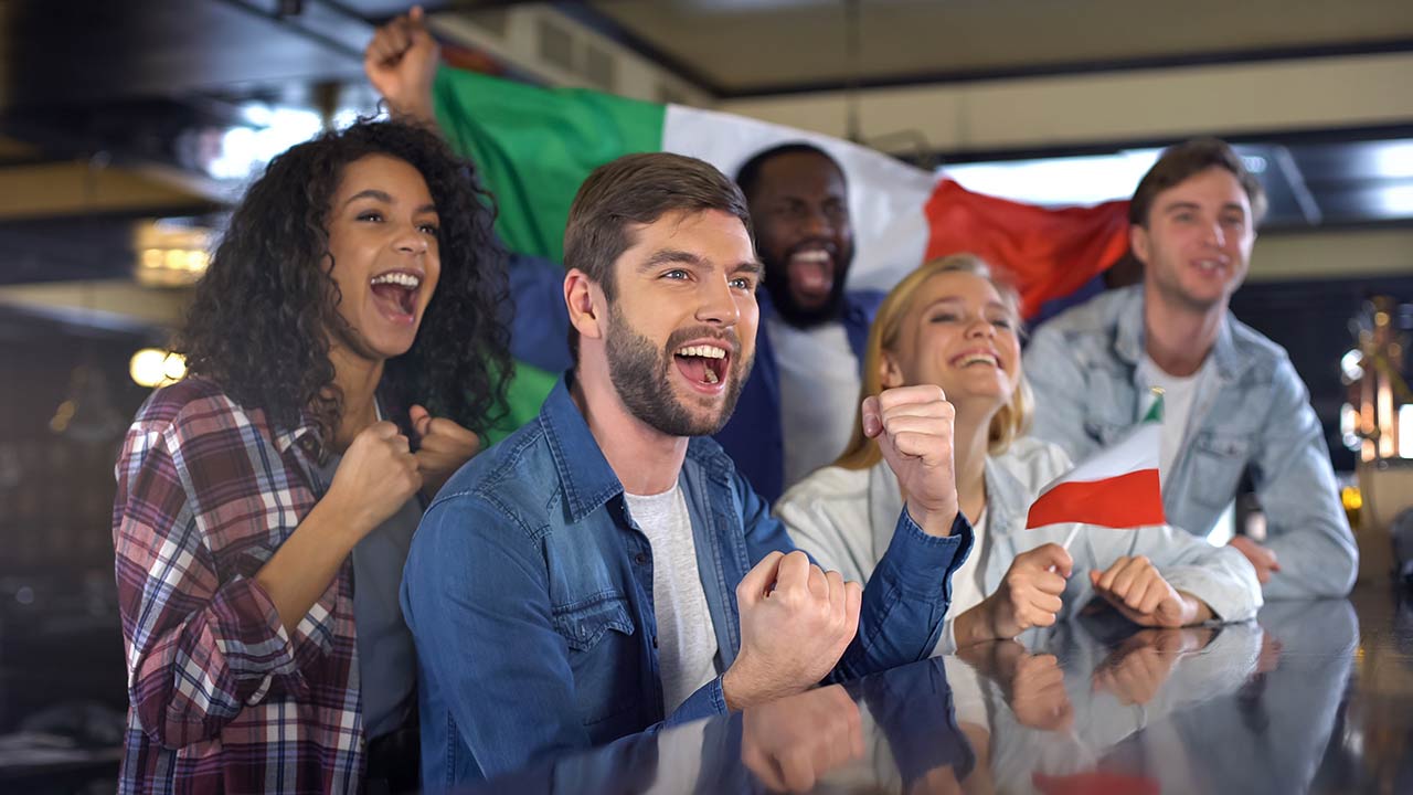 Photo of cheerful Italian fans holding flag celebrating winning match, happy time in bar