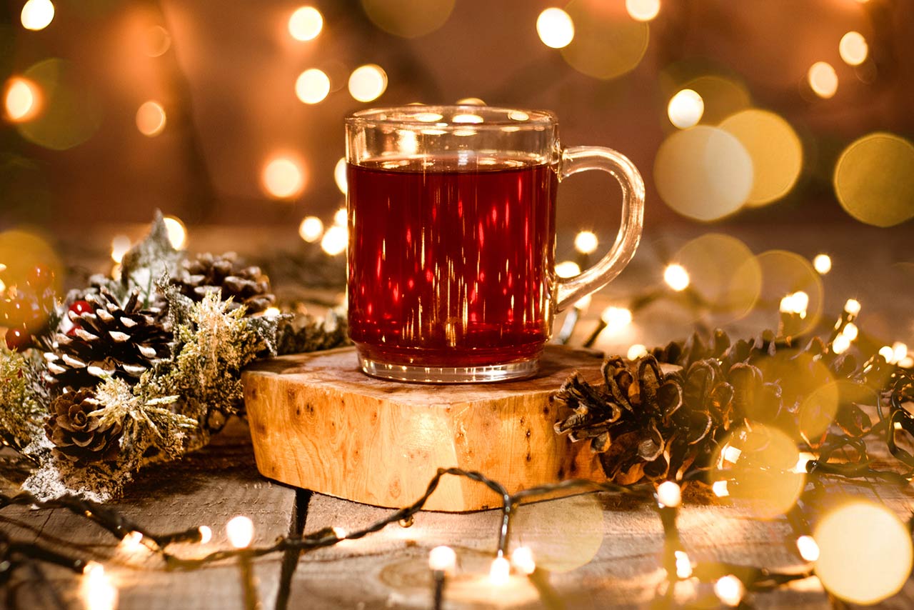 Photo of a holiday scene of a tea mug with decoration and bokeh lights on a wooden table and christmas lights