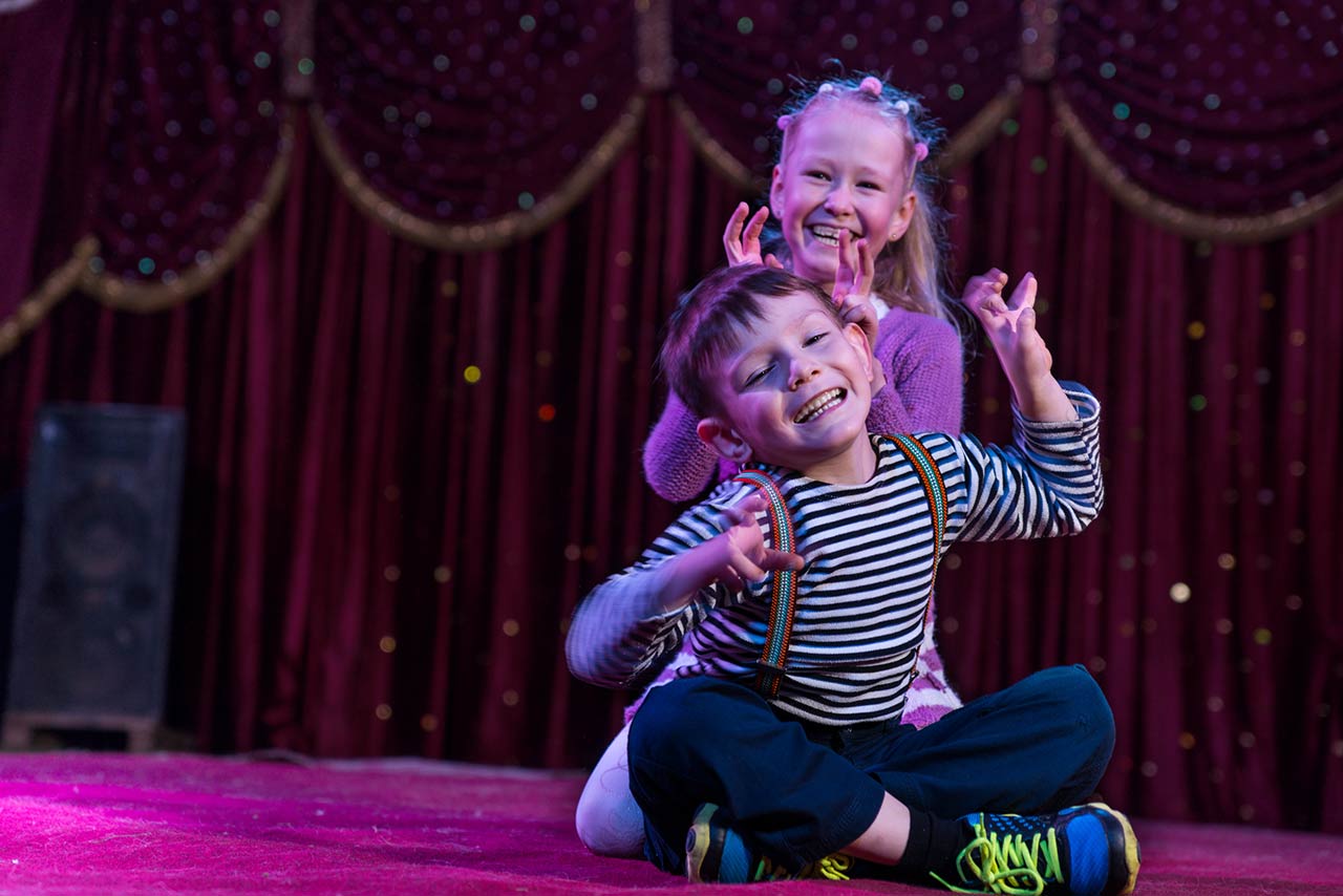 Photo of two funny playful children, boy and girl, smiling while acting as monsters with claws, on a purple stage, in a theatrical representation