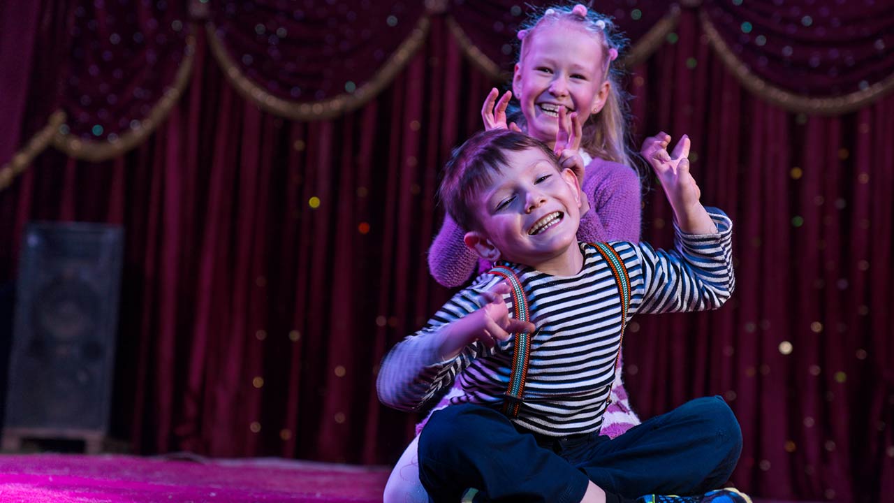 Photo of two funny playful children, boy and girl, smiling while acting as monsters with claws, on a purple stage, in a theatrical representation