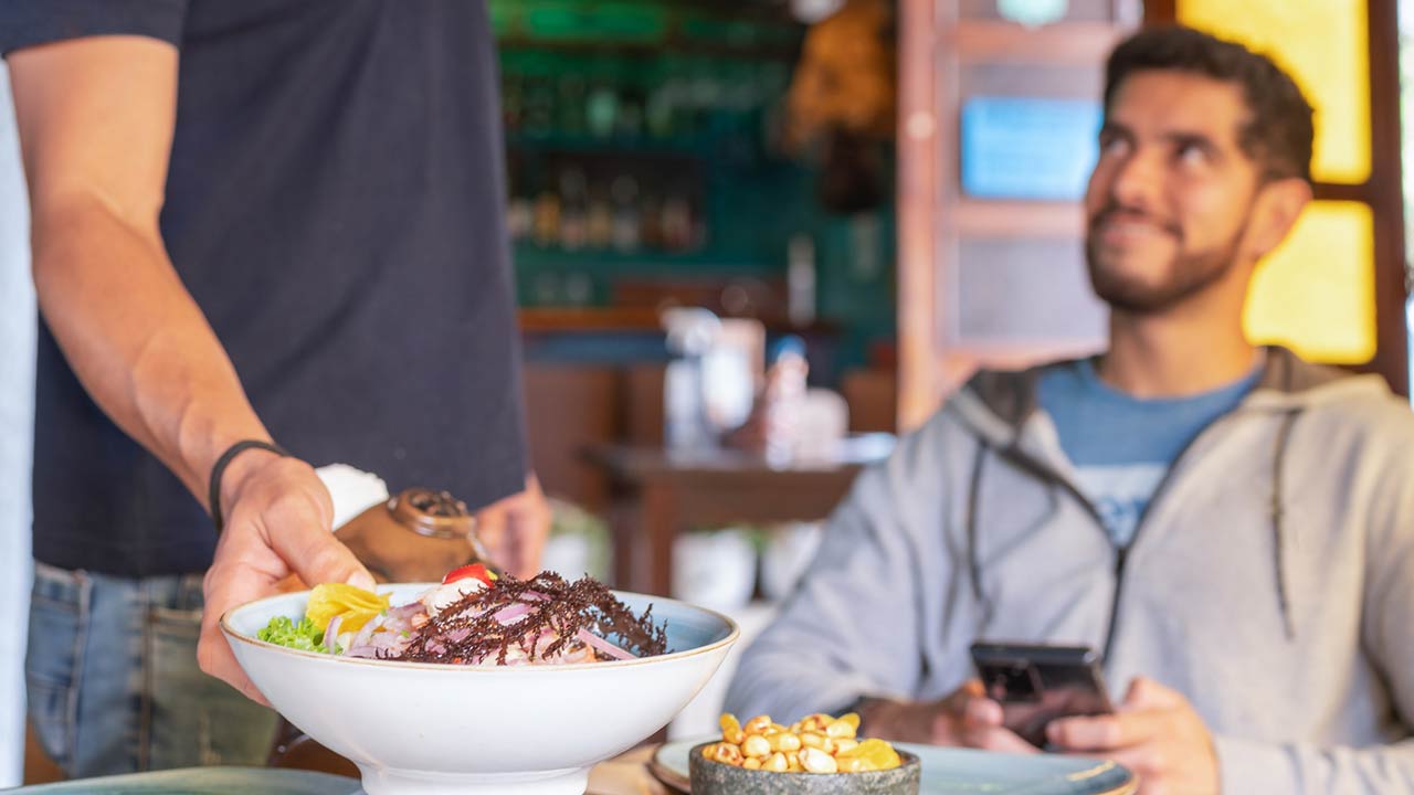 Photo of a waiter serving ceviche to a table with customers in a restaurant