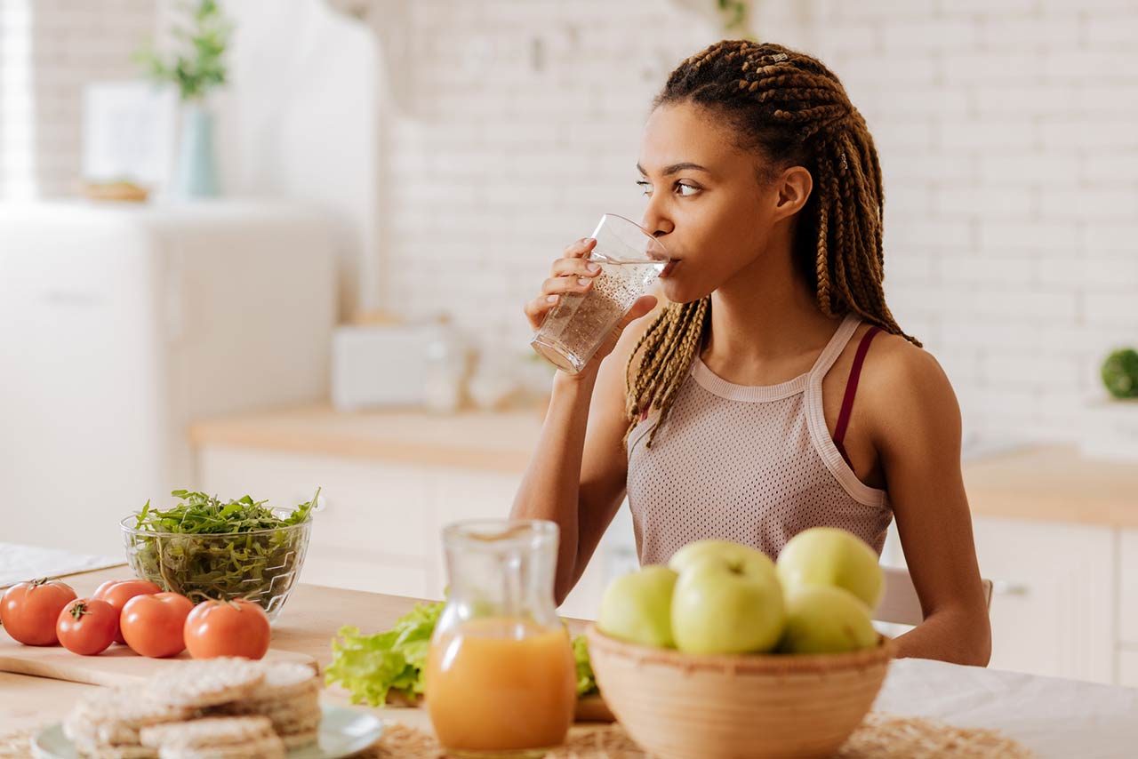 Photo of a slim and fit woman with many little braids drinking water before having breakfast