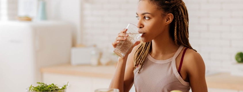 Photo of a slim and fit woman with many little braids drinking water before having breakfast