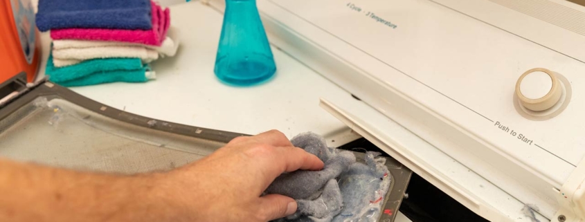 Photo of hand removing dirty lint screen of dryer while doing laundry