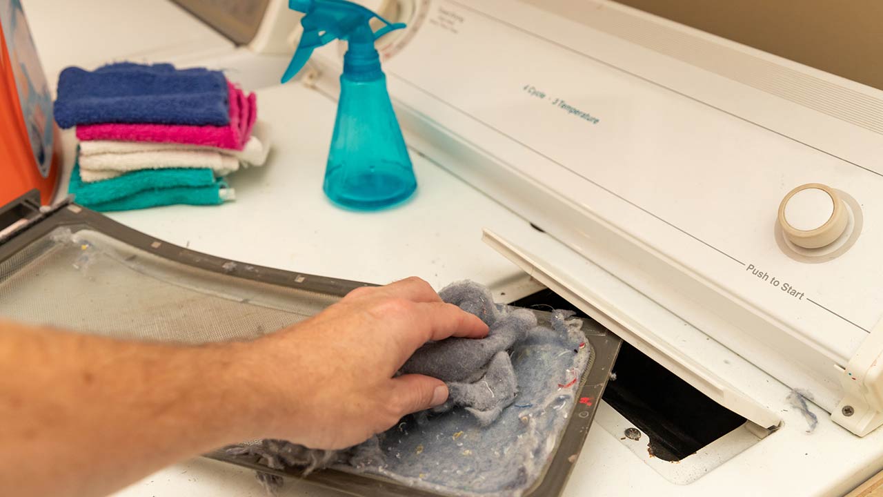 Photo of hand removing dirty lint screen of dryer while doing laundry