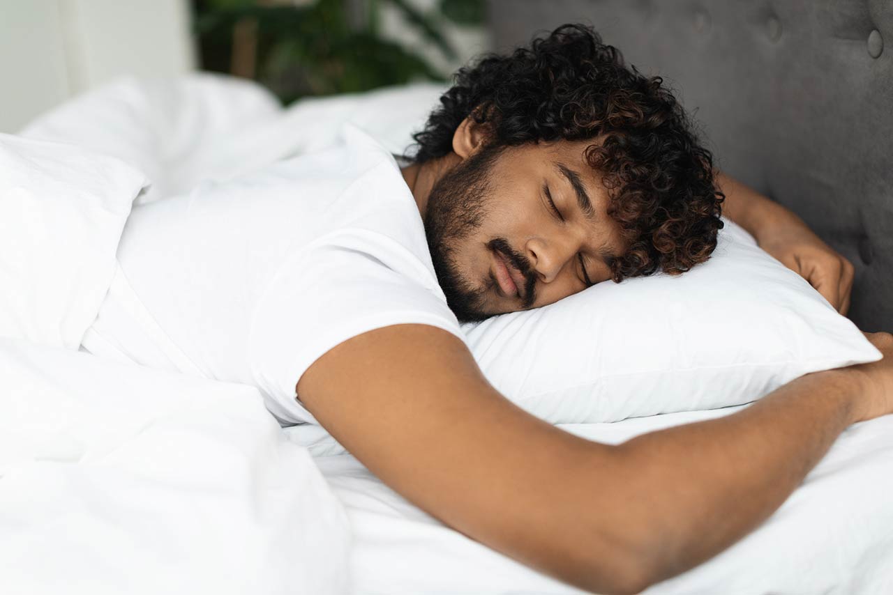 Closeup shot of peaceful young curly indian man sleeping in comfortable bed alone at home