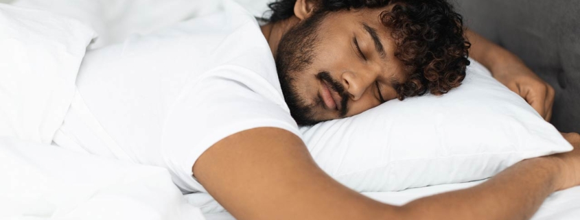 Closeup shot of peaceful young curly indian man sleeping in comfortable bed alone at home