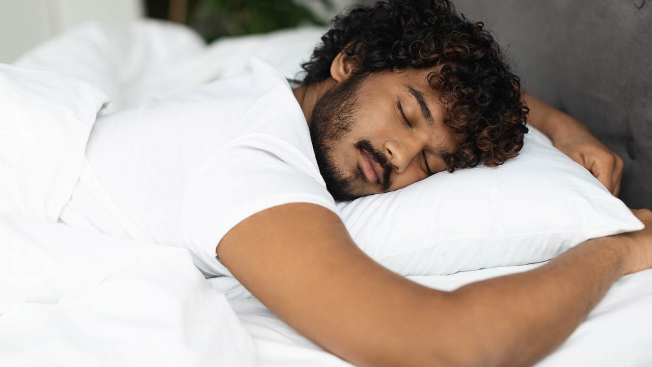 Closeup shot of peaceful young curly indian man sleeping in comfortable bed alone at home