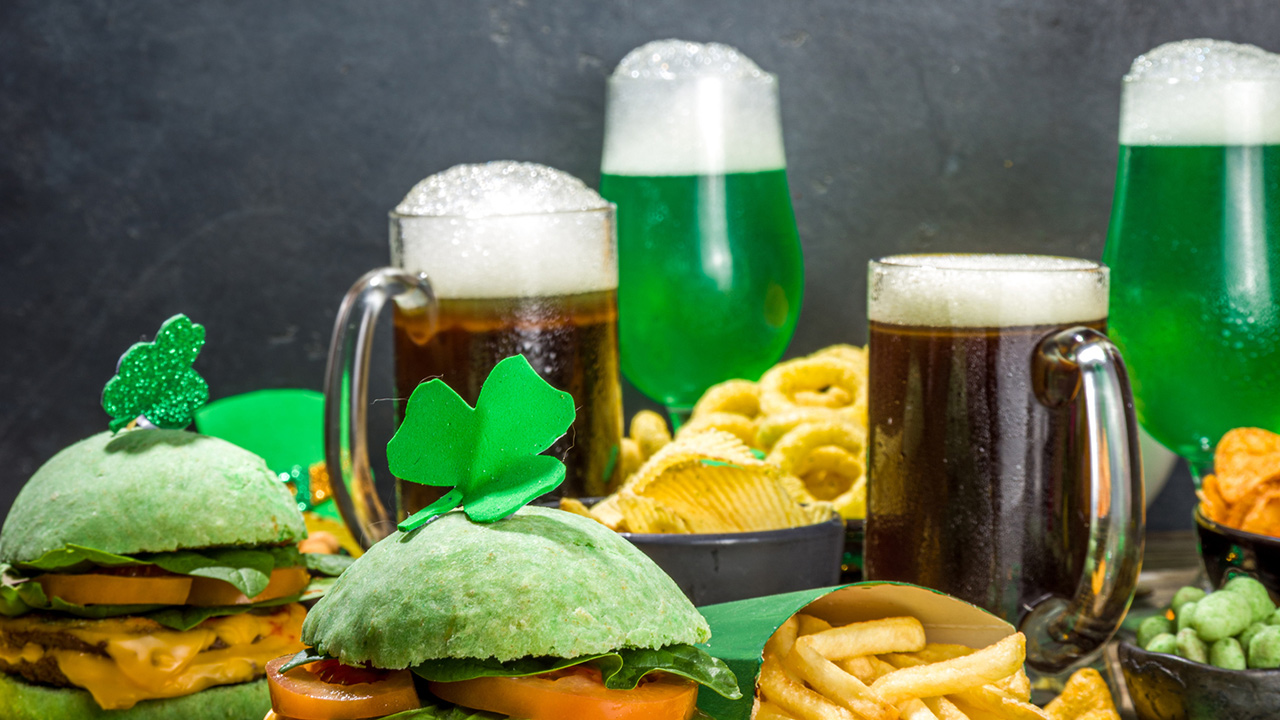 Irish St Patrick`s day beer, ale glasses, snacks, appetizer, green burger, wooden bar table with shamrock, clover, coins, leprechaun hat