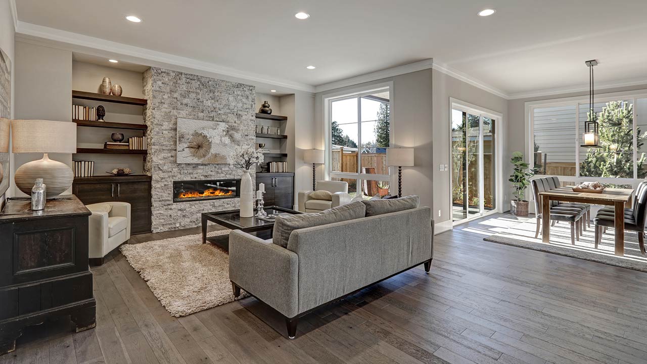 Living room interior in gray and brown colors features gray sofa atop dark hardwood floors facing stone fireplace with built-in shelves