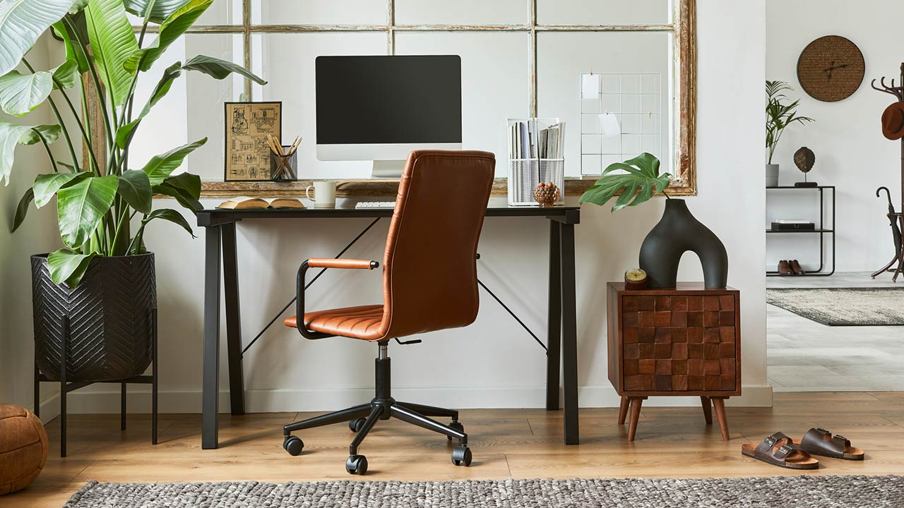 Creative composition of modern masculine home office workspace interior with black industrial desk, brown leather armchair, pc and stylish personal accessories