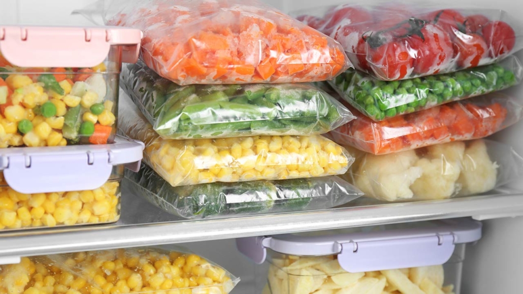 Plastic bags and containers with different frozen vegetables in refrigerator