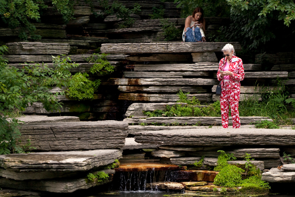Seated girl and standing funny colorfully dressed old lady at the Alfred Caldwell Lily Pool, Lincoln Park Conservatory