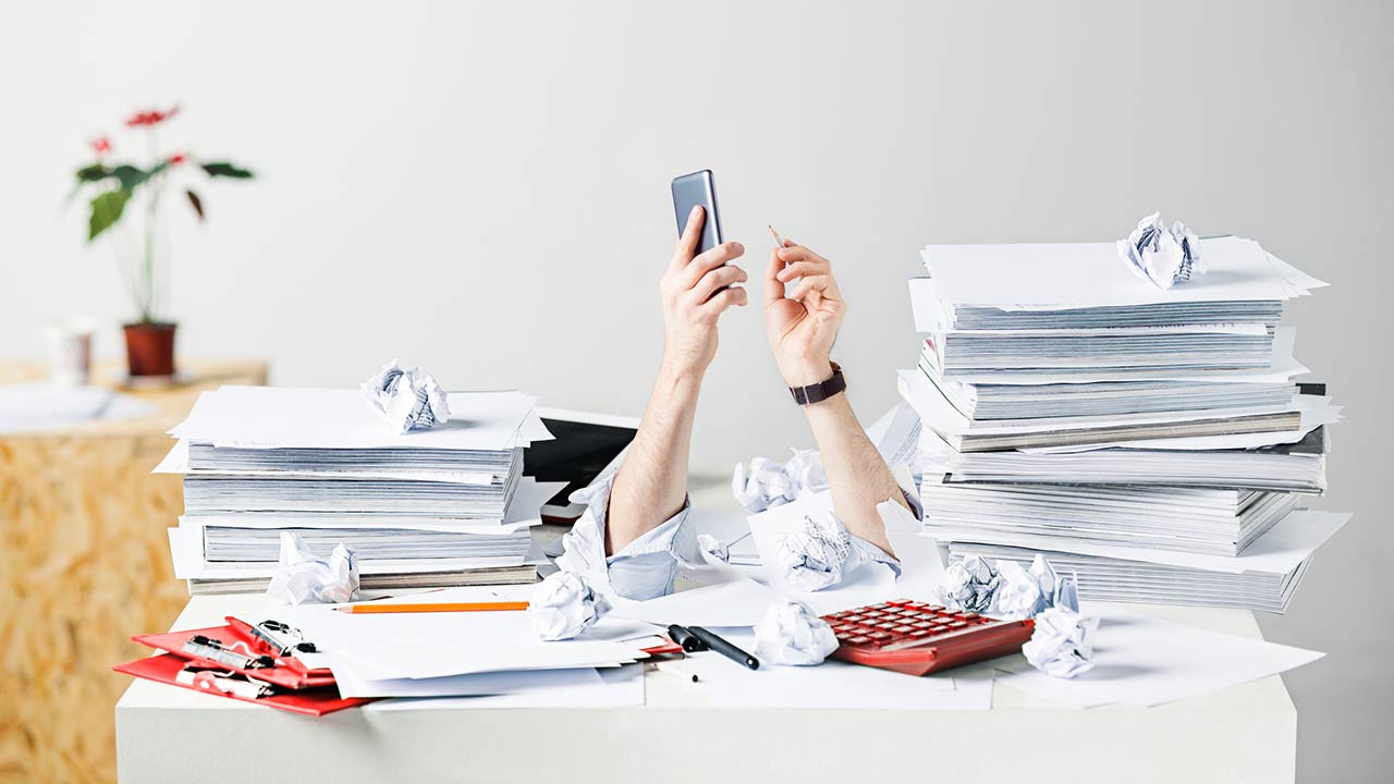 A conceptual image of many crumpled papers on the desk of a stressed male
