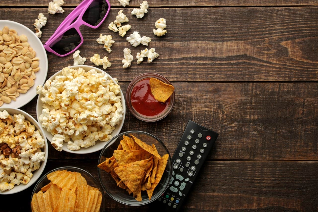 Popcorn and various snacks, 3D glasses, TV remote on a brown wooden background