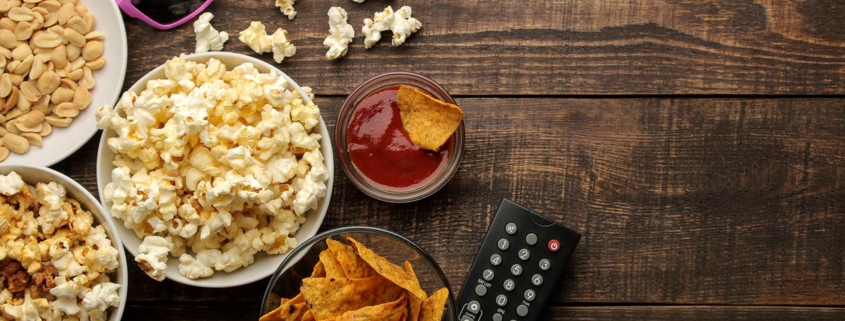 Popcorn and various snacks, 3D glasses, TV remote on a brown wooden background