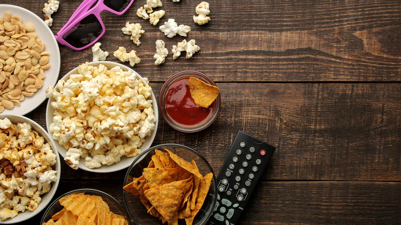 Popcorn and various snacks, 3D glasses, TV remote on a brown wooden background