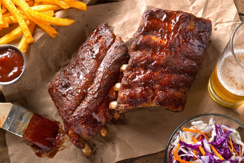 A rack of delicious baby back ribs with barbecue sauce, french fries, coleslaw and beer