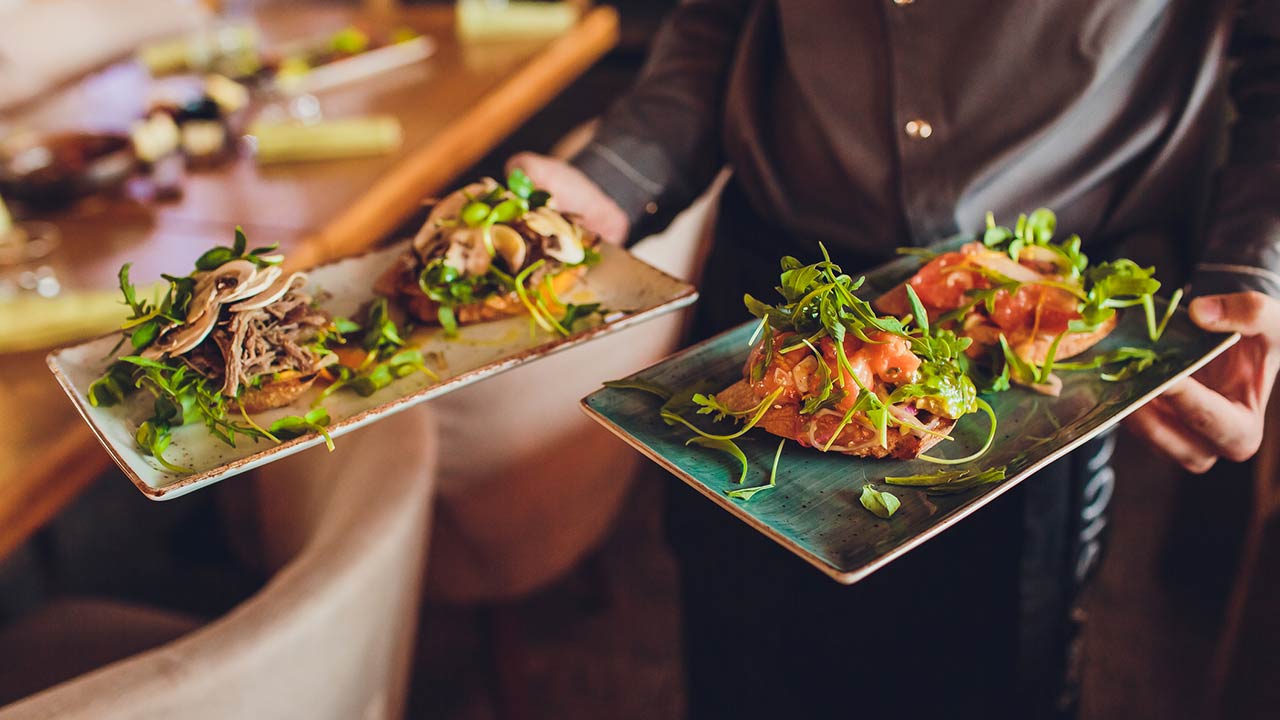 Two meat plates with salad leaves and a summer salad in waiter's hands