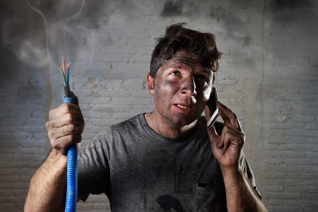 A young man holding a smoking electrical cable after electrical accident with dirty burnt face