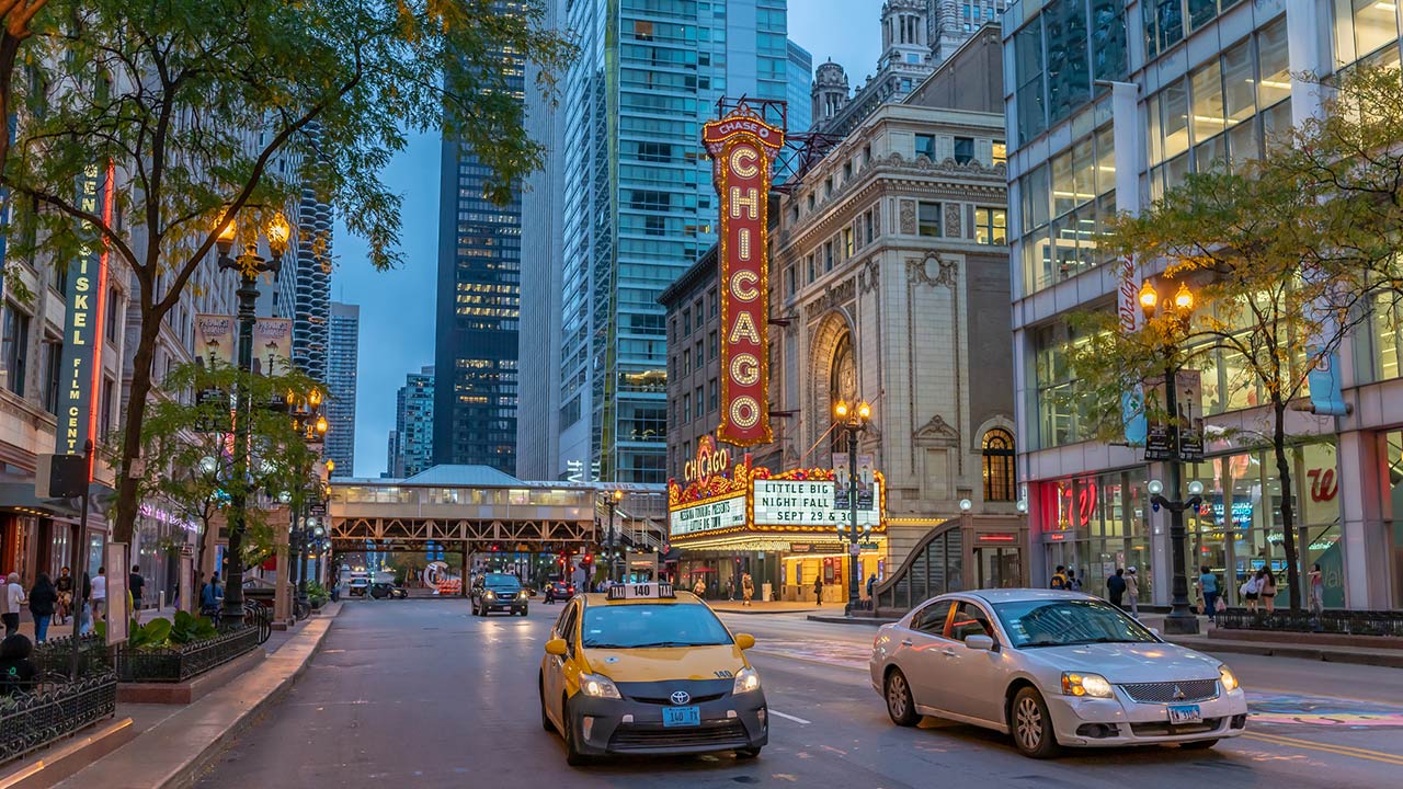 A taxi cab in focus downtown at night, with the Chicago Theater and the famous State Street beyond