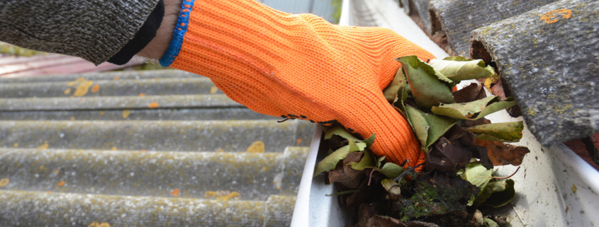 Roofer cleaning a rain gutter with an orange glove on