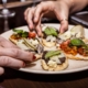 Two hands grabbing mini tacos off of a shared plate
