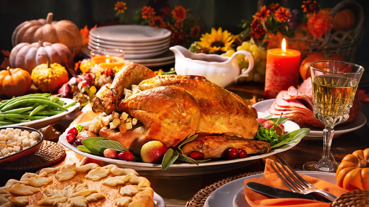 Roasted turkey garnished with cranberries on a rustic style table decoraded with pumpkins, vegetables, pie, flowers, and candles