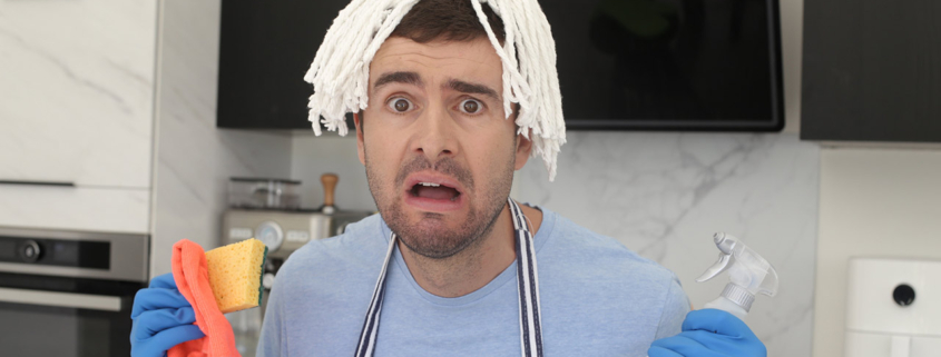 A very distraught man trying to clean the kitchen with a mop on his head