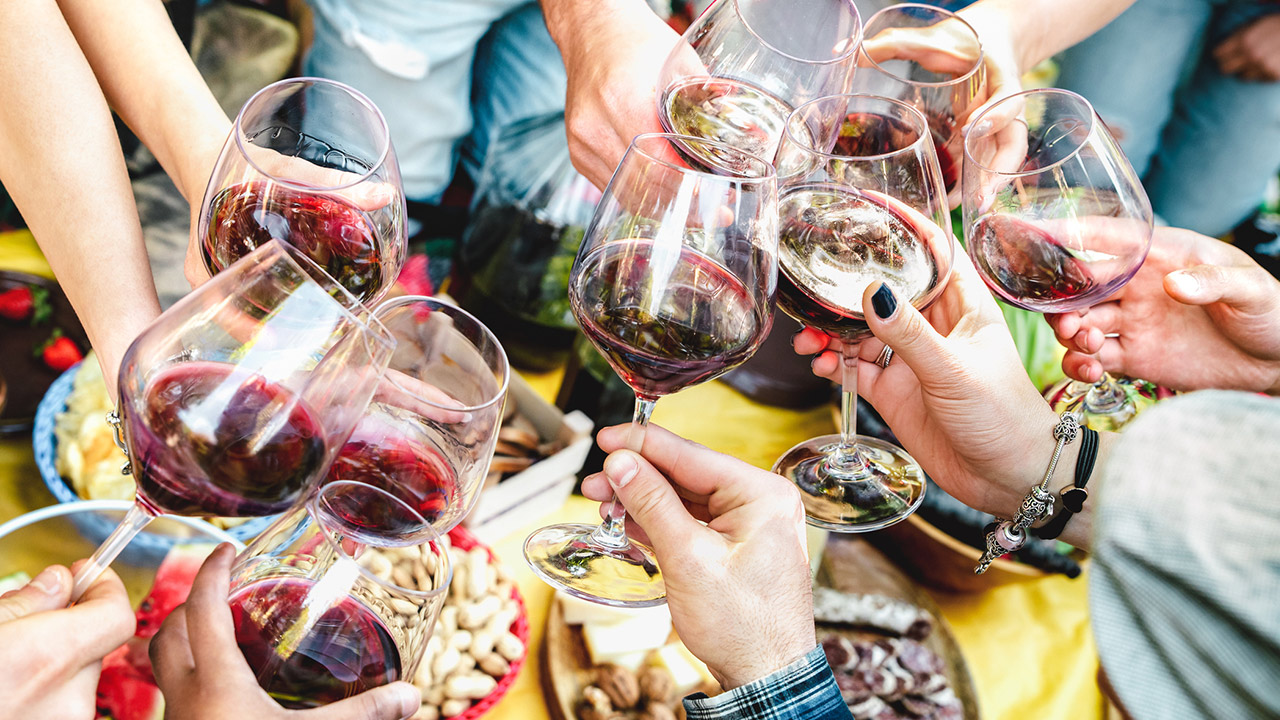 People hands toasting red wine and having fun out side cheering at winetasting experience