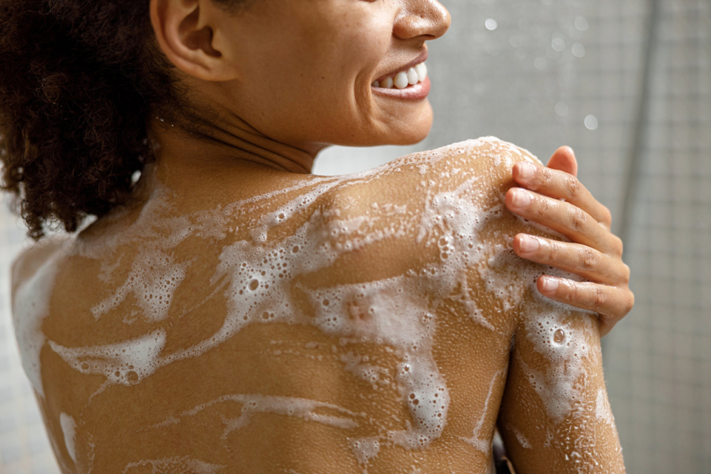 Close up of african woman taking a shower with gel or shampoo foam in bathroom