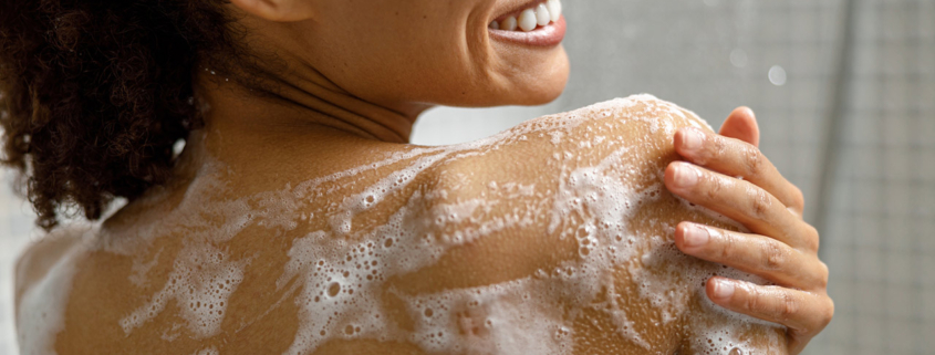 Close up of african woman taking a shower with gel or shampoo foam in bathroom