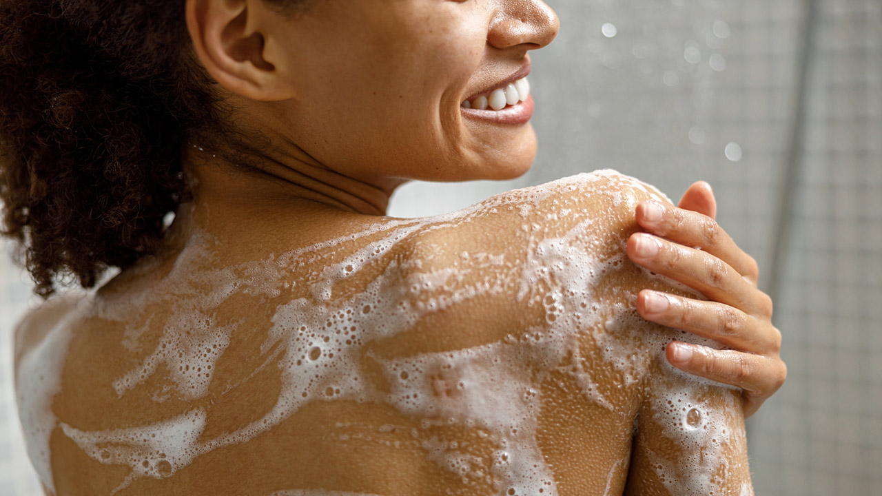 Close up of african woman taking a shower with gel or shampoo foam in bathroom