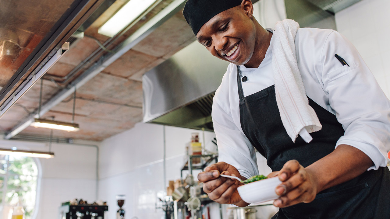 Happy male cook wearing apron standing by kitchen counter preparing food