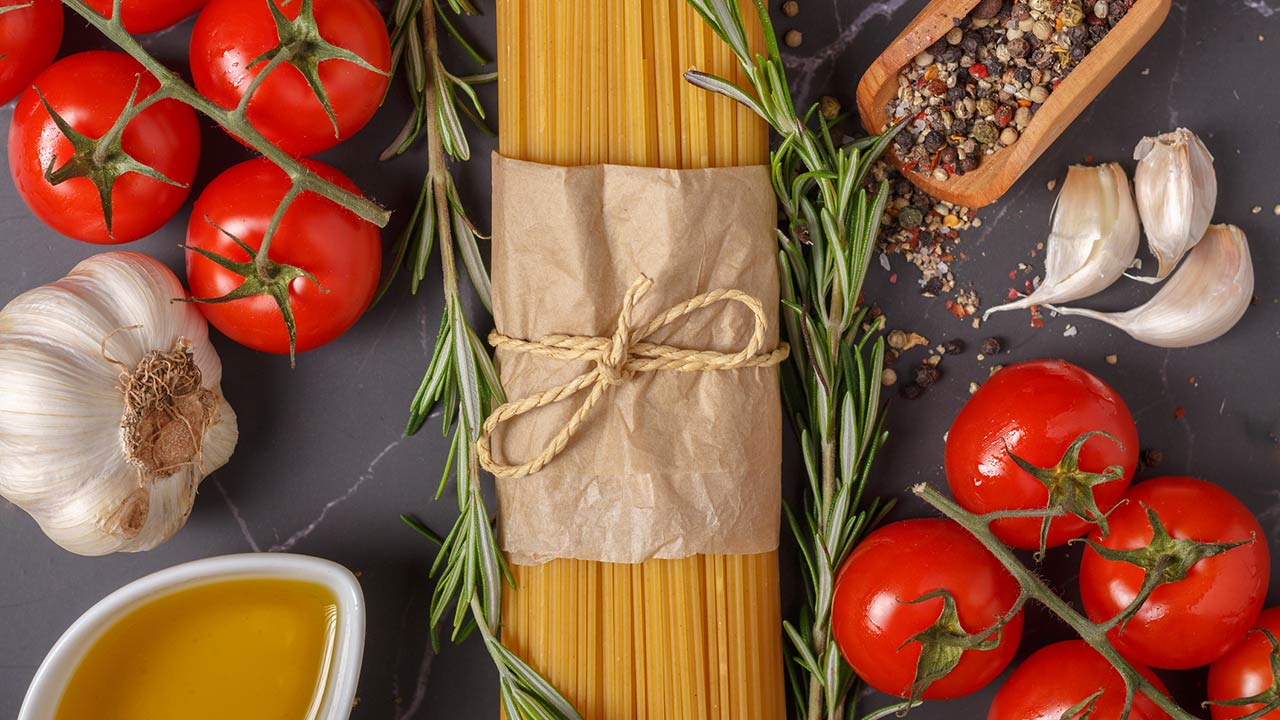 Spaghetti, tomatoes, olive oil, garlic and rosemary on dark gray marble kitchen table