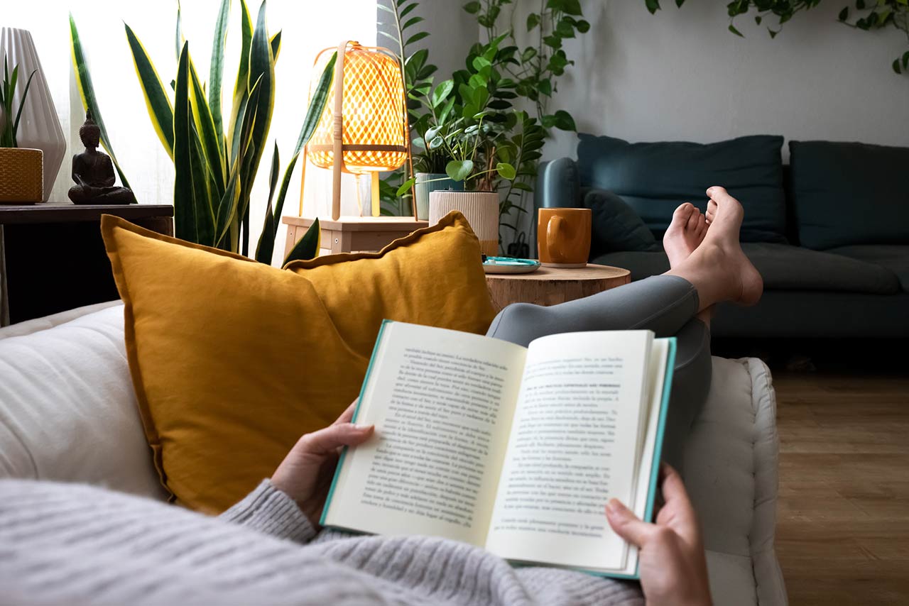 young woman relaxing at home reading a book lying on sofa