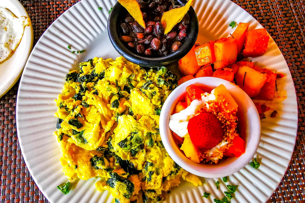 Mexican breakfast with scrambled eggs with spinach fruit and potatoes nicely arranged on white plate