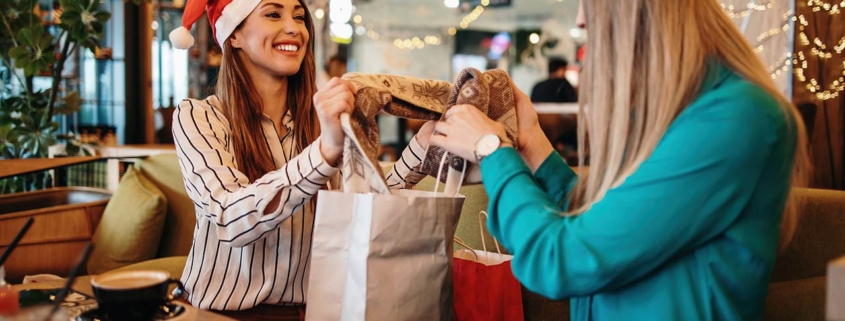 Two best friends in a nice restaurant exchanging presents wearing Christmas hats
