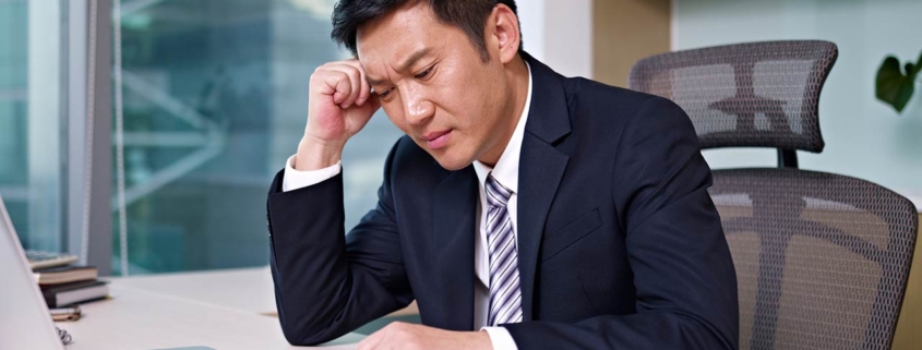 Asian businessman sitting and thinking in office, looking frustrated