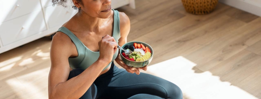 Athletic woman eating a healthy fruit bowl while sitting on floor in the kitchen at home