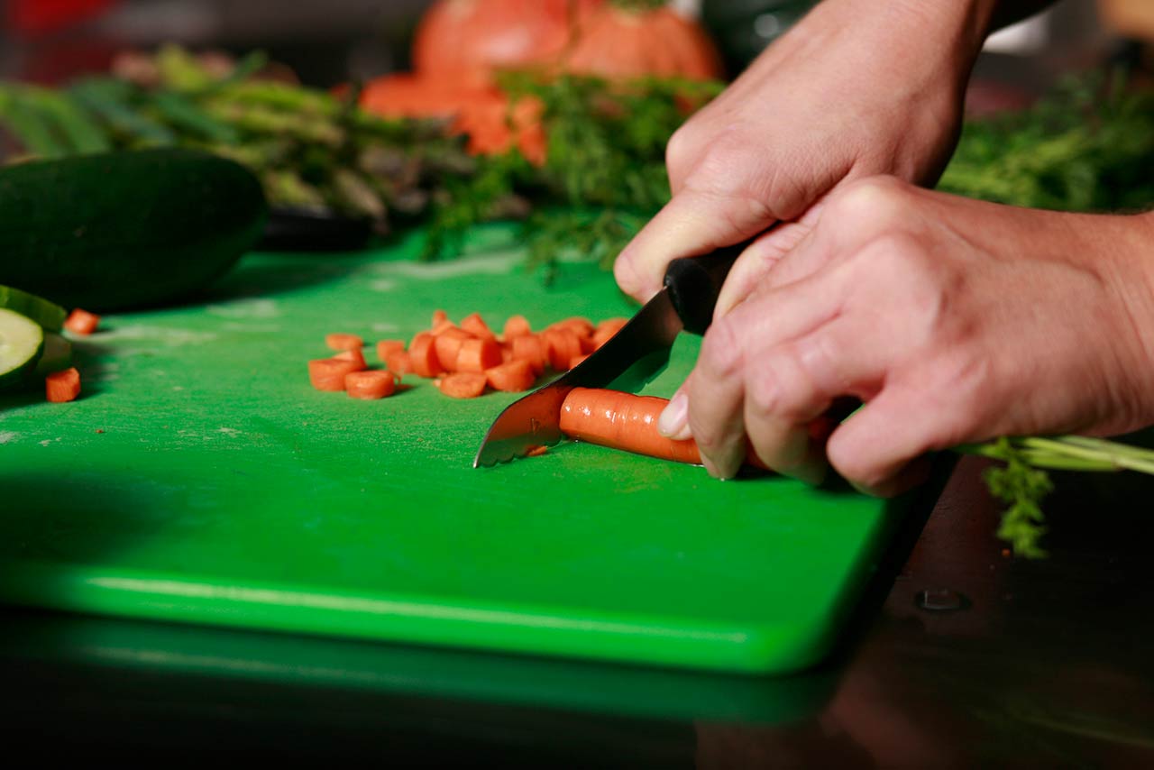 hands cutting a carrot on a green cutting board