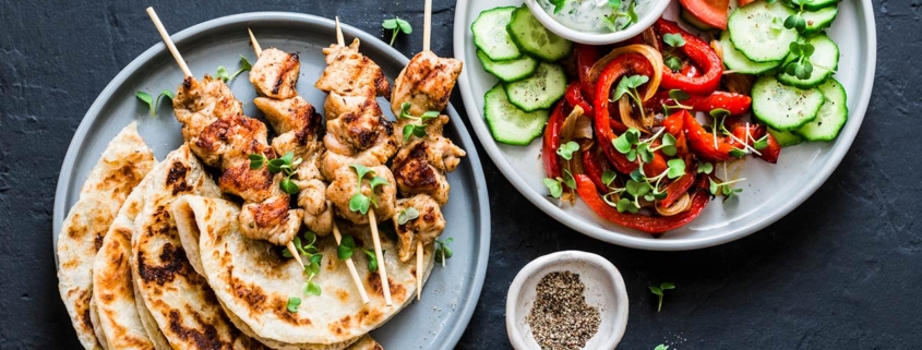 skewers, flatbread, tomatoes, cucumber salad, baked sweet pepper, yogurt herb sauce on a dark background