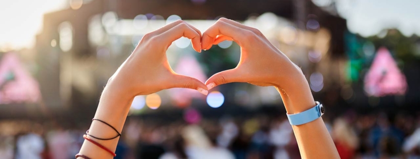 Hands shape heart sign at sunset beach music fest, crowd enjoys live concert