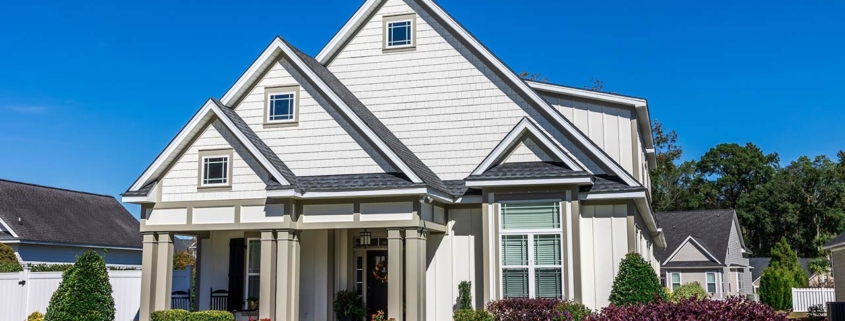 The front view of a new construction cottage craftsman style white house with a triple pitched roof