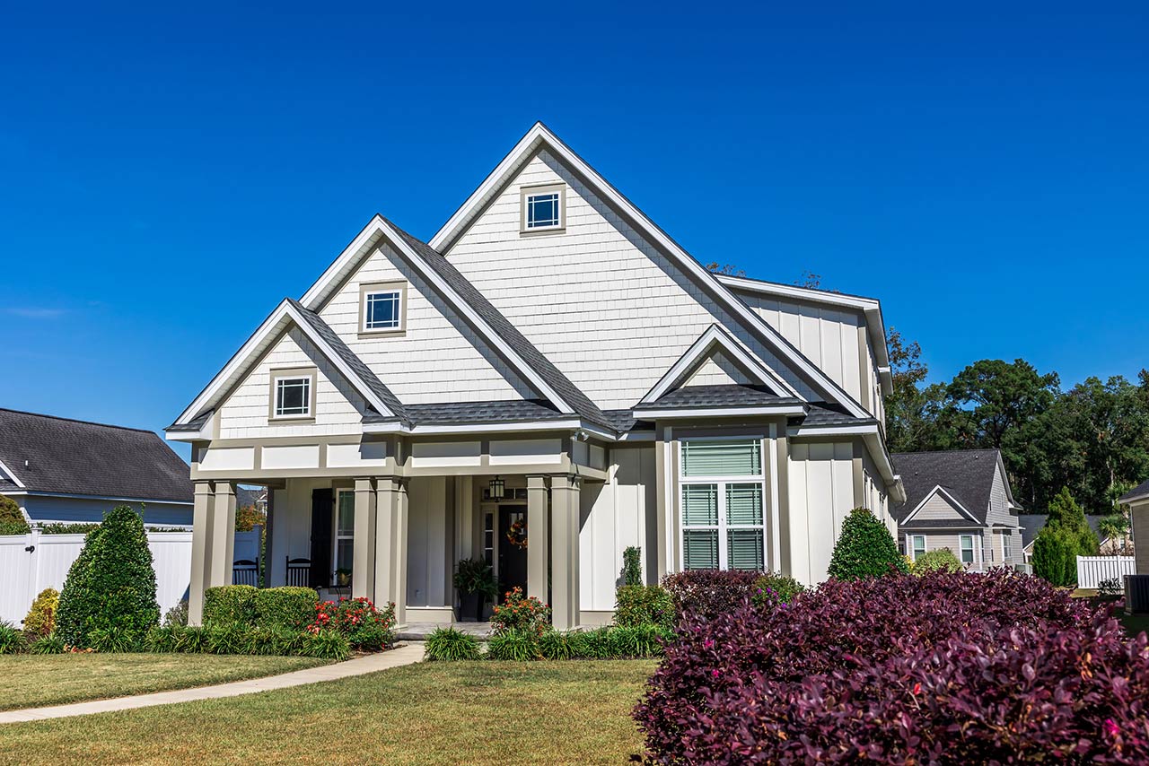 The front view of a new construction cottage craftsman style white house with a triple pitched roof