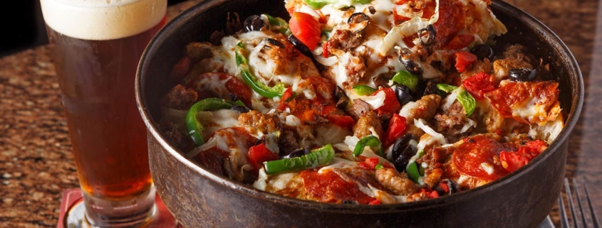 Freshly made deep dish pizza in the pan served with beer