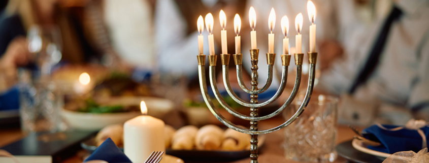 Lit candles in menorah with extended Jewish family in the background on Hanukkah