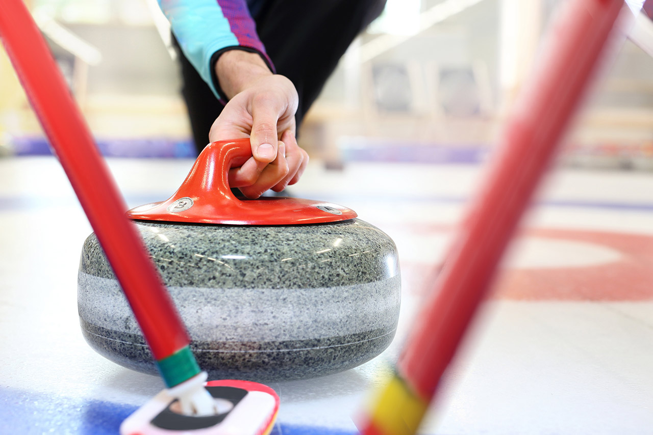 Curling player is brushing the ice by directing the stone to the house